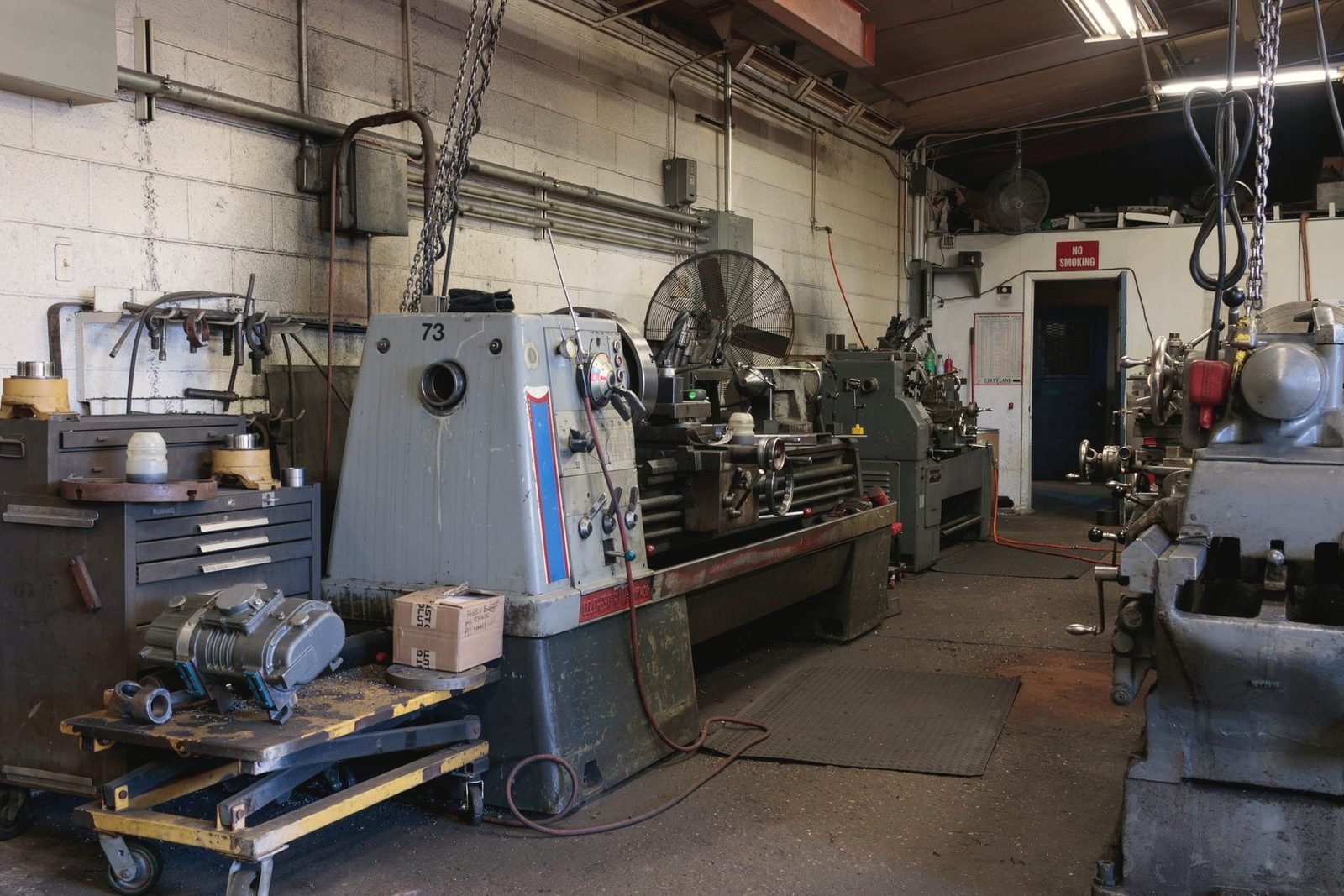 Machine shop floor with lathes, drill presses and hoists under fluorescent light