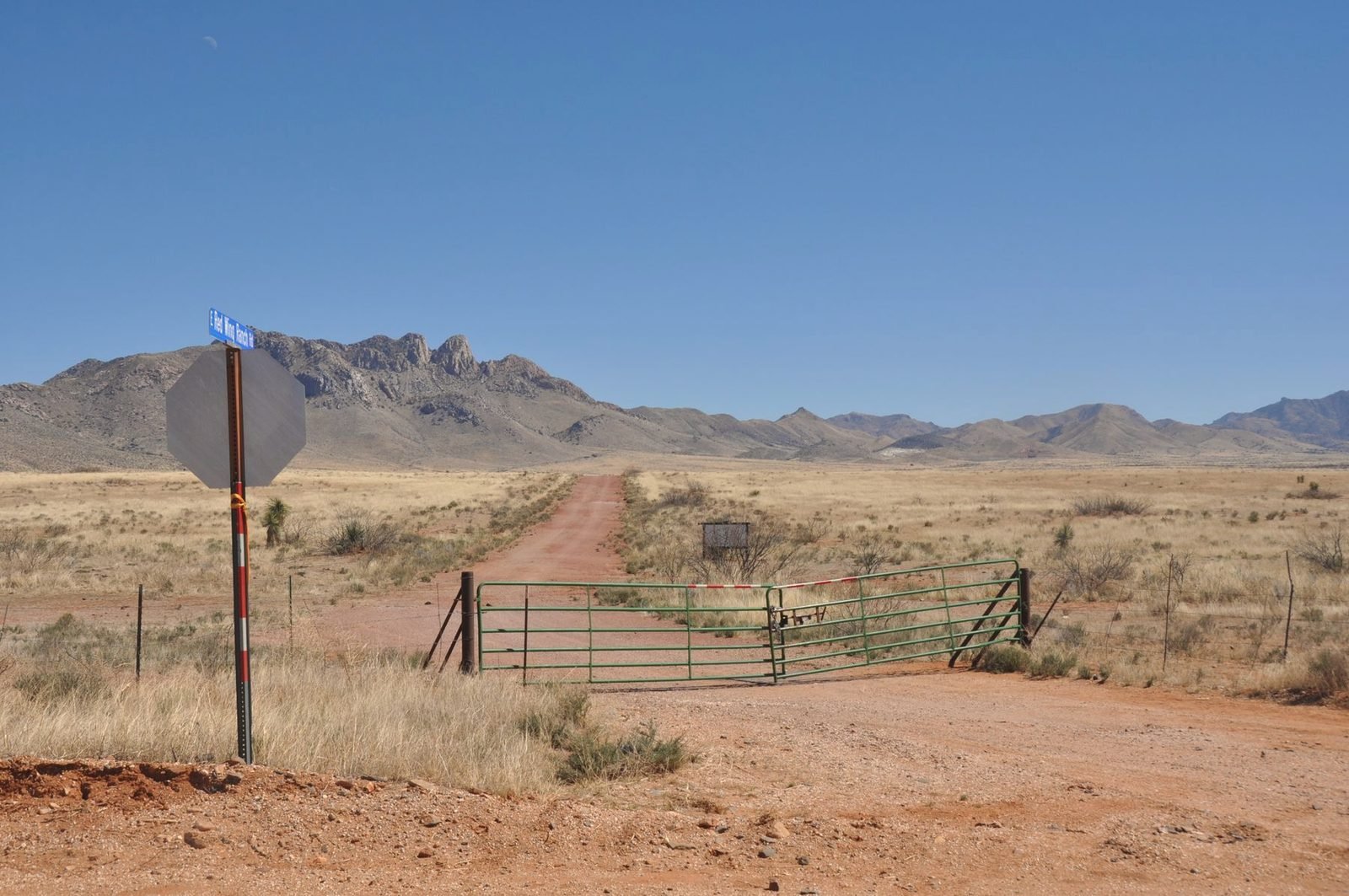 Red dirt road and cattle gate running toward desert mountains in West Texas