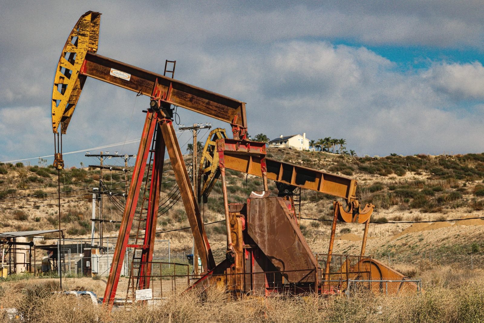 Rust-colored pumpjack working beside a second unit on a scrubby hillside