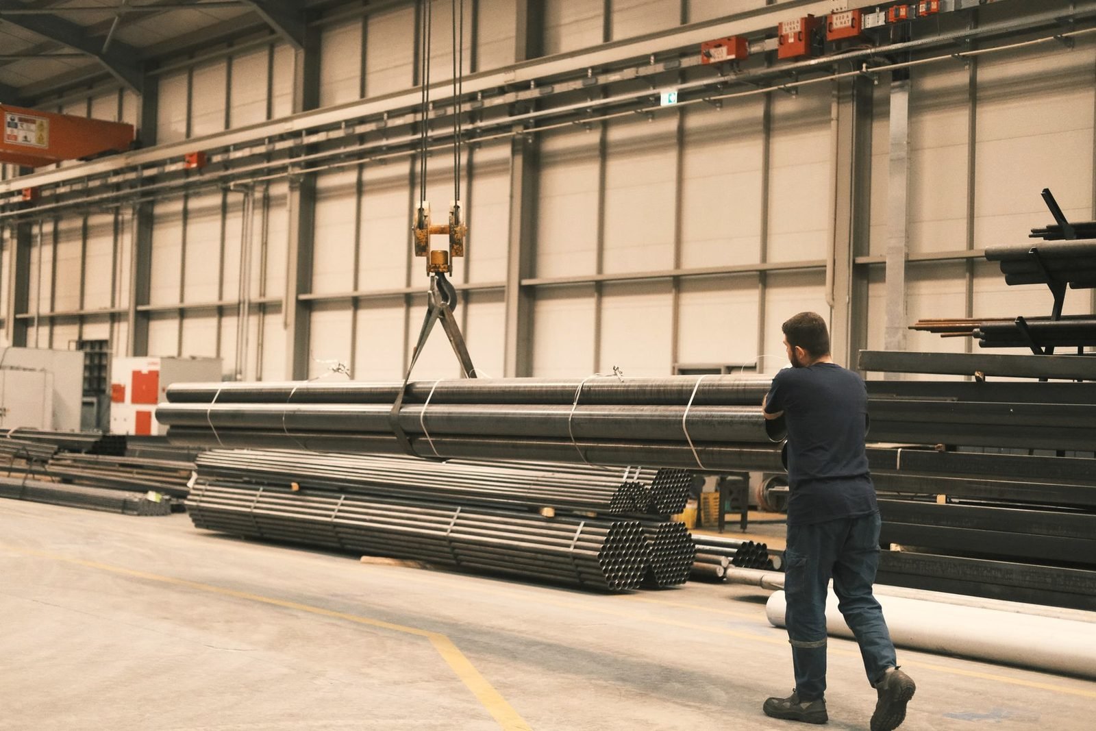 Worker seen from behind strapping steel pipe on a warehouse rack